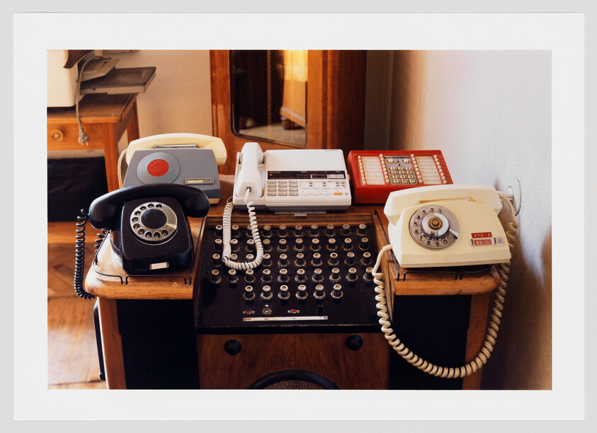 Several vintage rotary and push-button telephones arranged on an old wooden telephone switchboard.