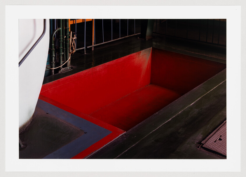 Deep empty red rectangular pit set into a dark industrial floor on a ship.
