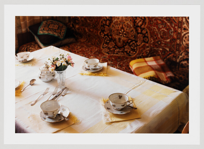 A small table set for tea with porcelain cups, saucers, silverware, and a flower vase.