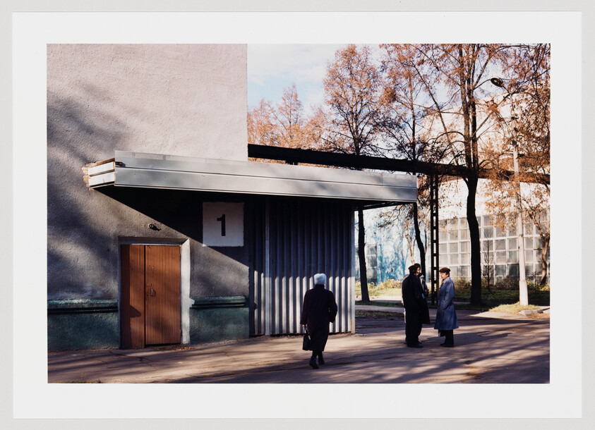 Three people stand and talk near a numbered industrial loading bay under an overhang.
