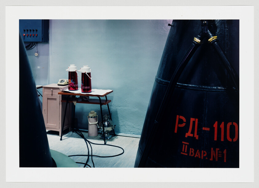 Large industrial tanks labeled РД-110 stand beside a small table holding thermoses and equipment.