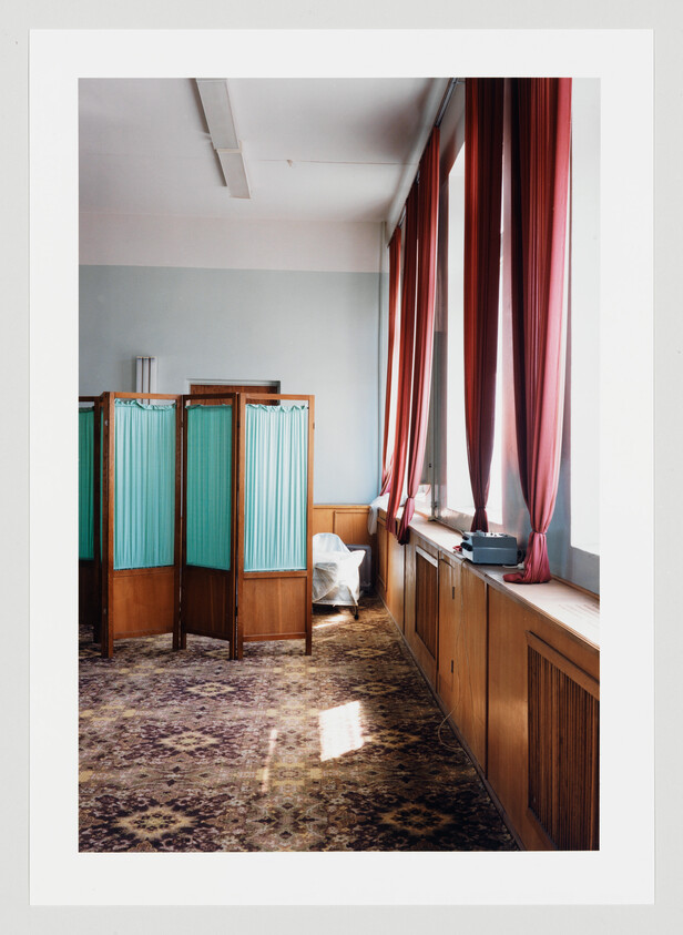 A quiet examination room with teal privacy screens, tall red curtains, and a covered chair.