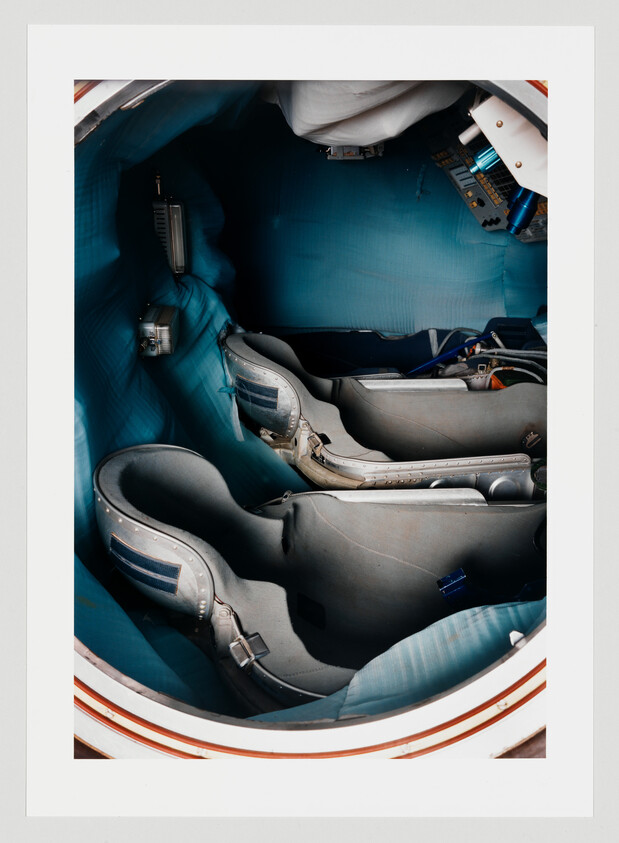 Two molded spacecraft seats secured inside a small blue crew capsule.