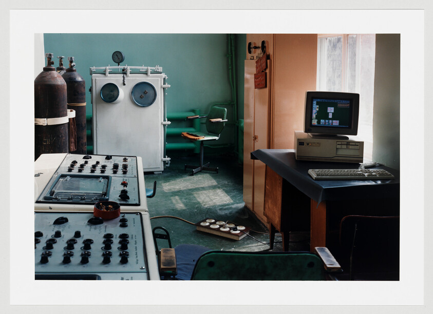 A vintage control room with analog panels, gas cylinders, and an old desktop computer on a desk.