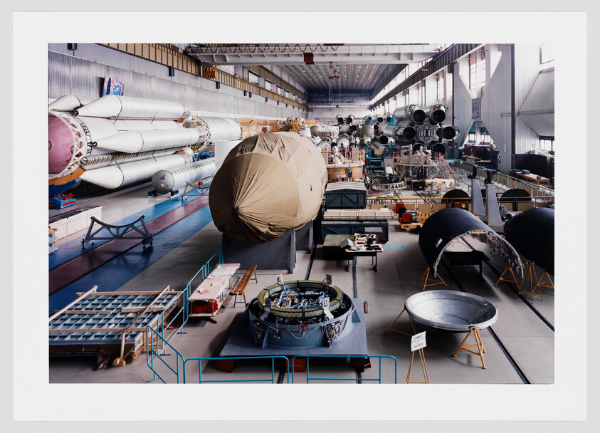 Large factory floor with rocket stages and spacecraft components under assembly and storage.