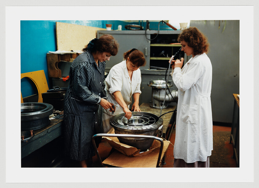 Three women inspect and assemble a large metal bearing in a factory workshop.