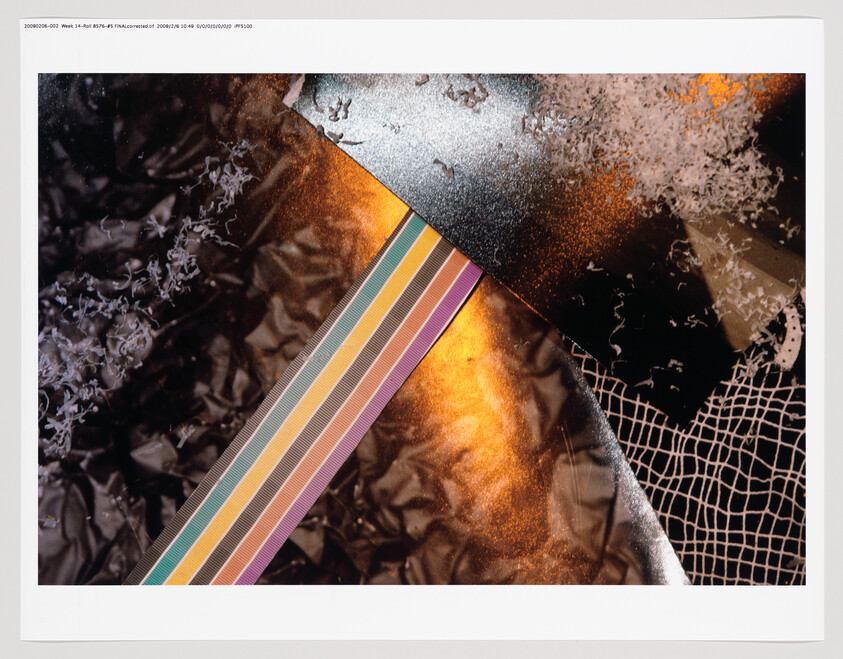 A close-up photograph of various textures and materials, featuring crumpled metallic surfaces in black and orange tones, with a strip of colorful stripes intersecting the image diagonally. There are also white shavings scattered across the surfaces, and a portion of a grid-like pattern is visible on the right side. The image has a white border framing it.