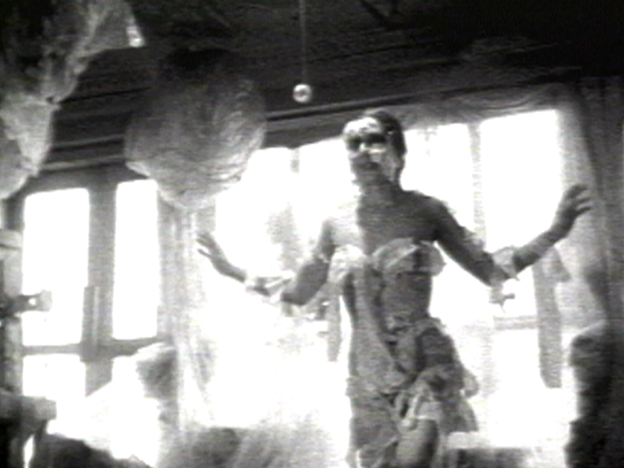 Person wrapped in web-like material stands in a dimly lit room with large windows.