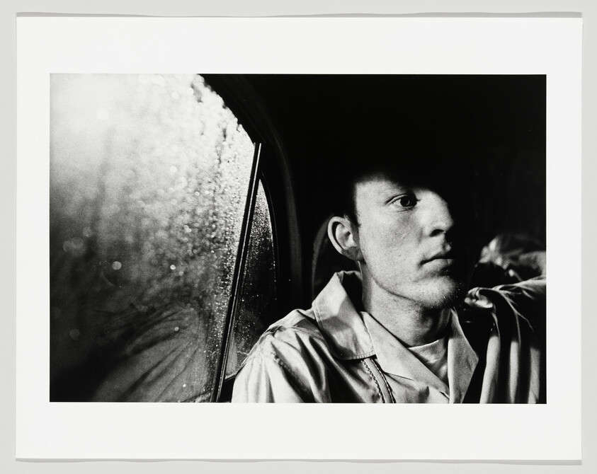 Young man sits in a car at night, staring out a rain-speckled window.