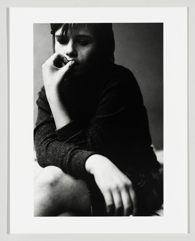 Young person sitting with hand to mouth, looking thoughtful and withdrawn.