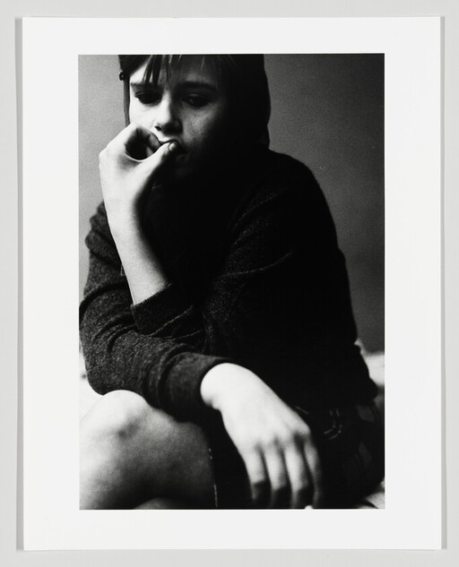 Young person sitting with hand to mouth, looking thoughtful and withdrawn.
