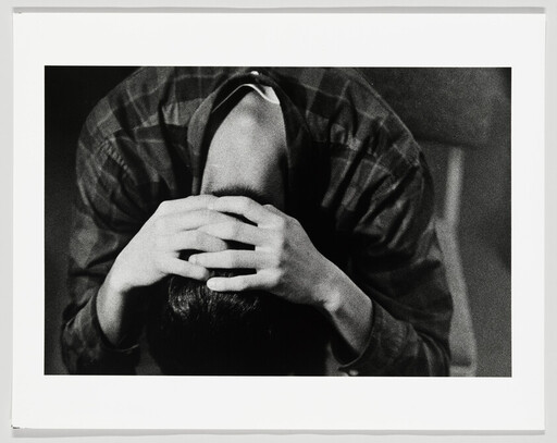 A person bent forward with hands clasped over their head, appearing distressed.