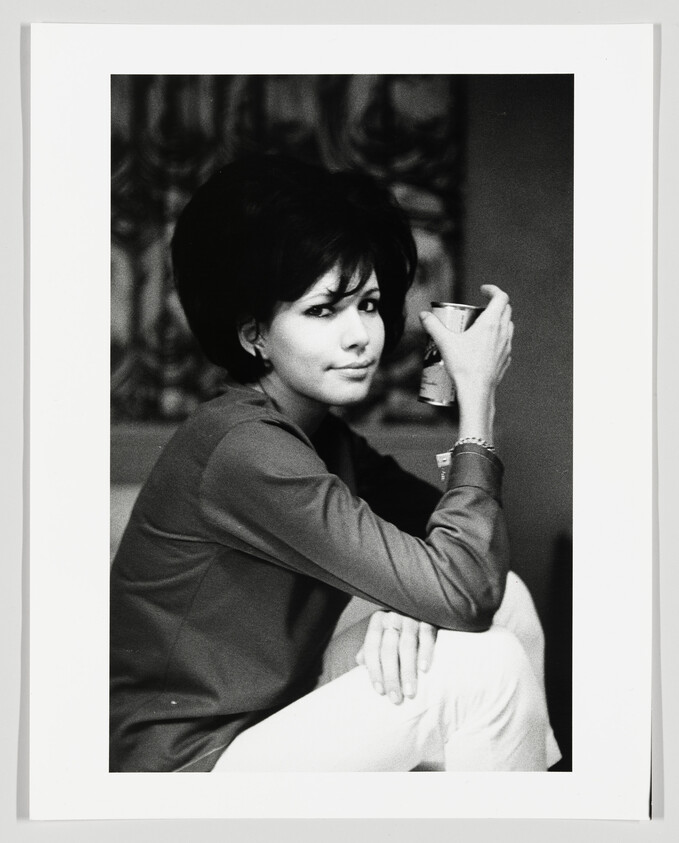 Young woman sitting with one knee up, holding a beverage can and looking toward the camera.