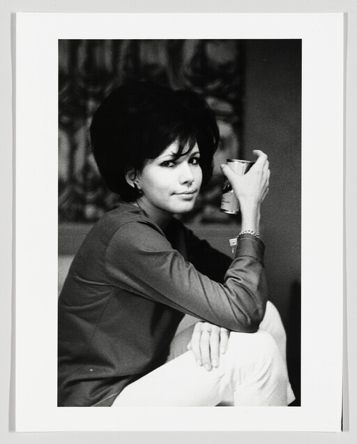 Young woman sitting with one knee up, holding a beverage can and looking toward the camera.