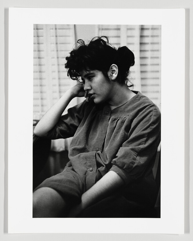 Young person sitting with head resting on hand, looking down pensively.