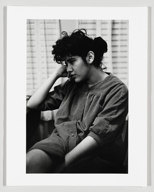 Young person sitting with head resting on hand, looking down pensively.