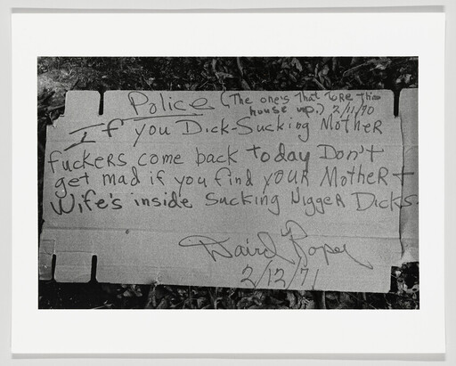 Handwritten cardboard sign threatening violence and using racist, sexually explicit language.