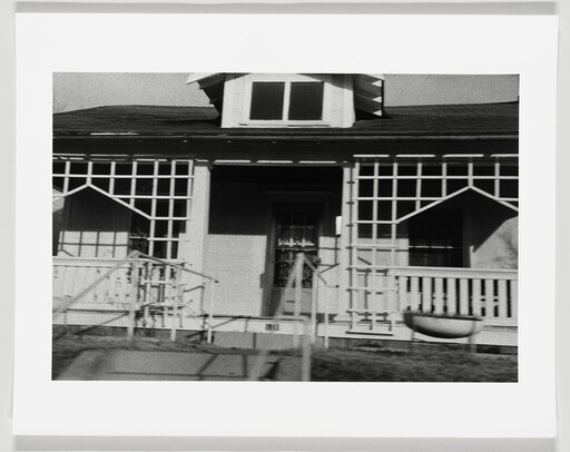 Front porch of a small house with lattice-work railings and a central doorway.