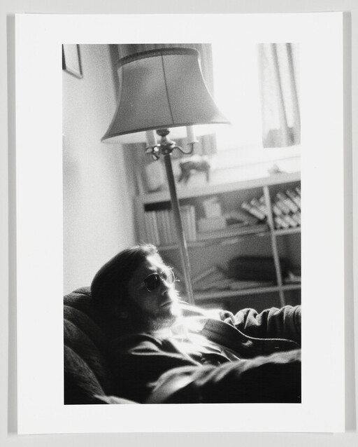 A person wearing sunglasses reclines on a couch under a floor lamp in a living room.