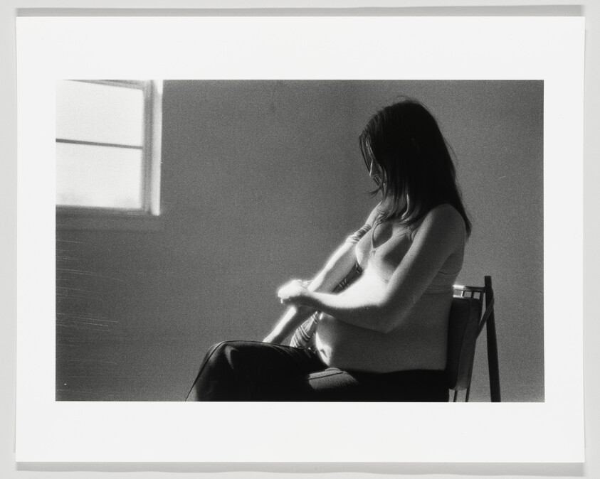 Pregnant woman sitting in a chair gently holding her belly while looking down.