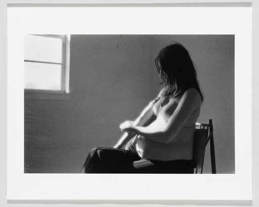Pregnant woman sitting in a chair gently holding her belly while looking down.