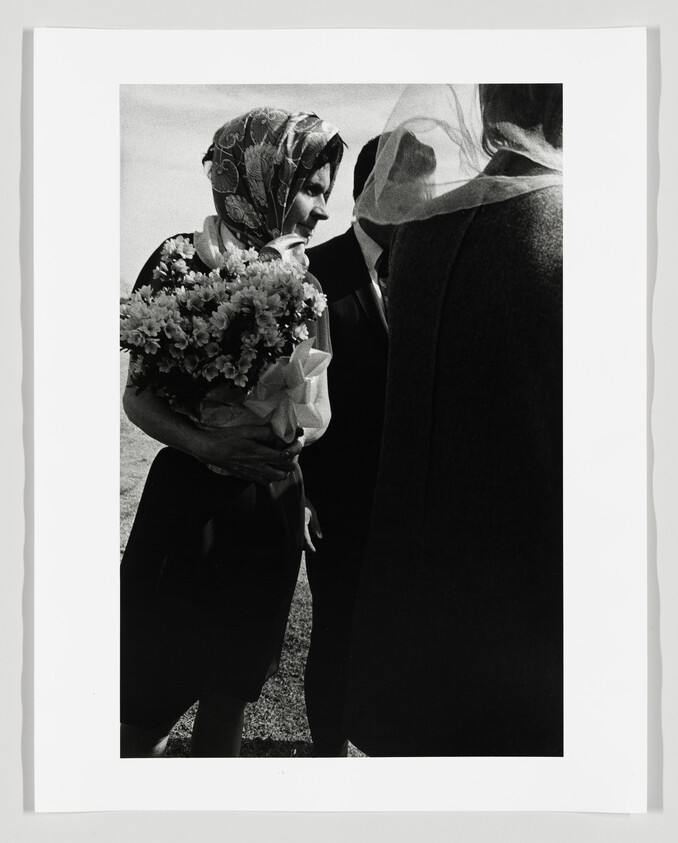 Woman wearing a patterned headscarf holds a large bouquet while talking to two people.