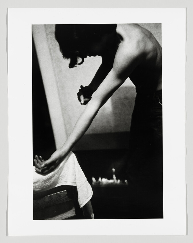 A shirtless person leans forward and extends their arm over a towel-covered bench.