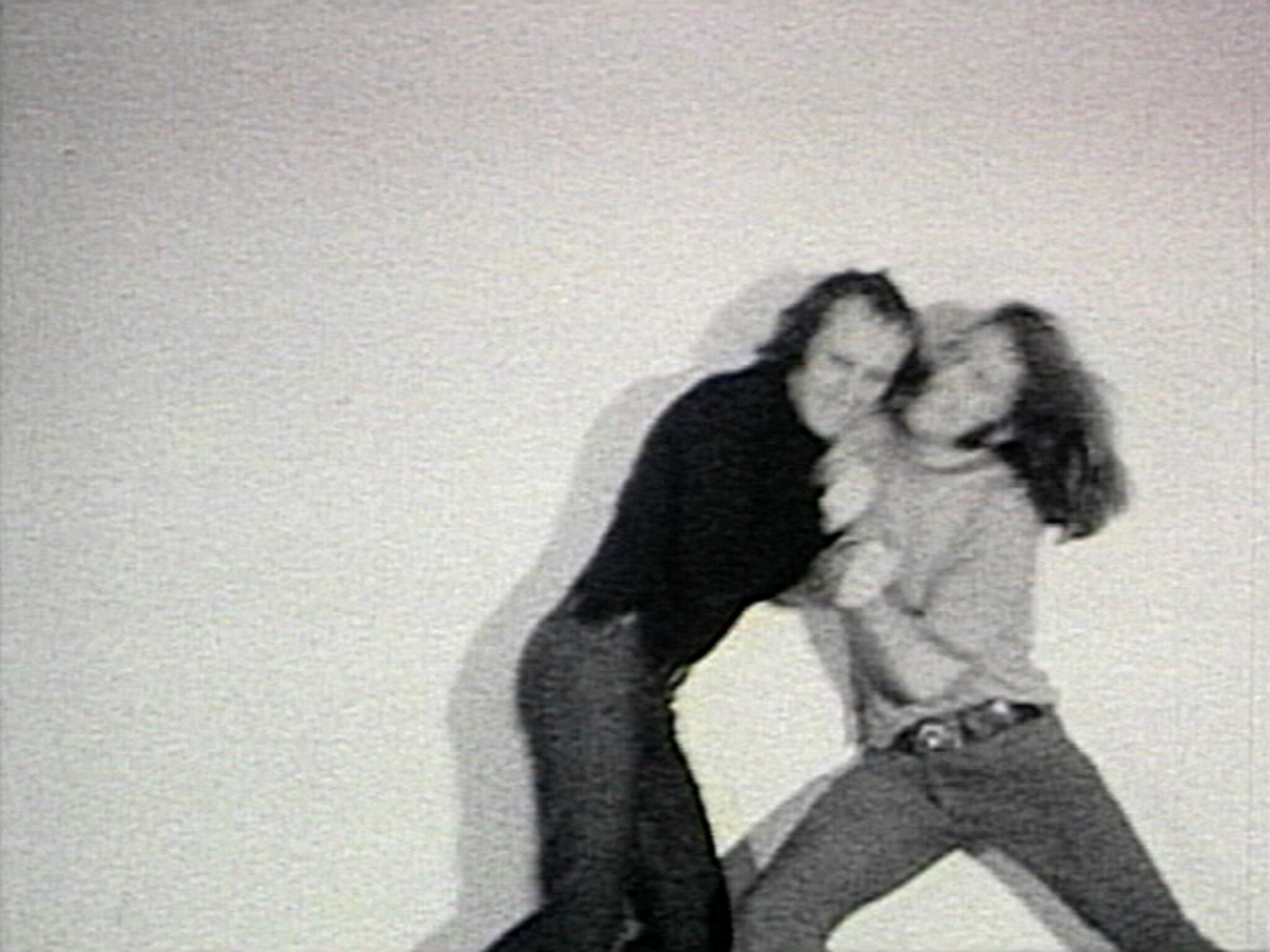 Two people stand close together, appearing to struggle or wrestle, with blurred motion against a plain background.