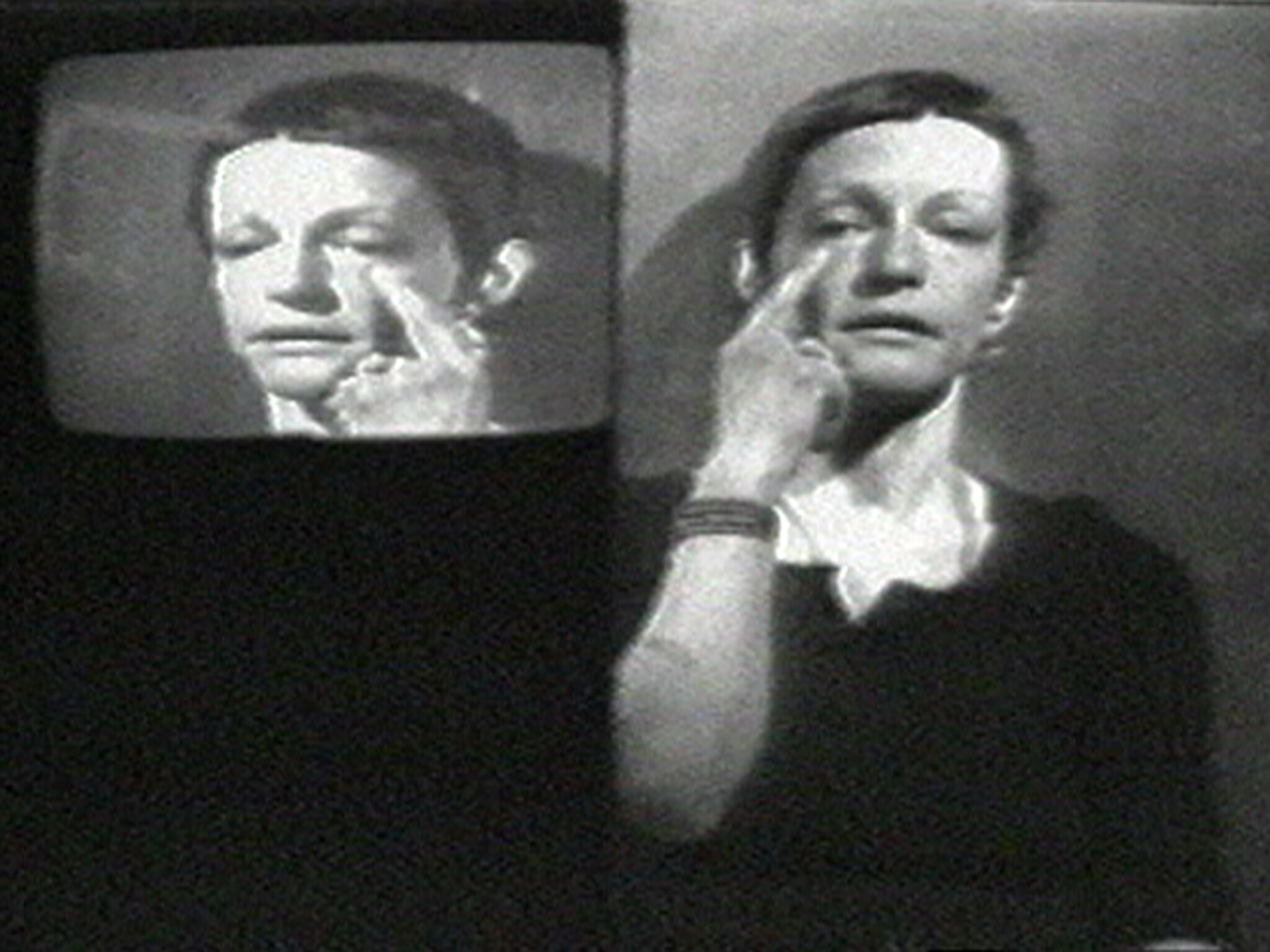 Woman on screen touches under her eye with finger while a smaller monitor shows the same gesture.