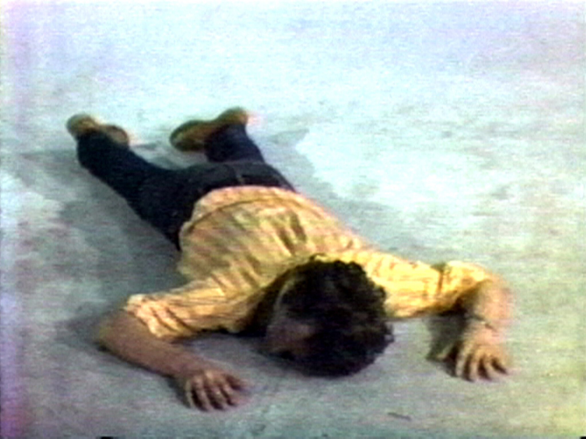 A person lies face down on a light-colored floor with arms stretched outward.