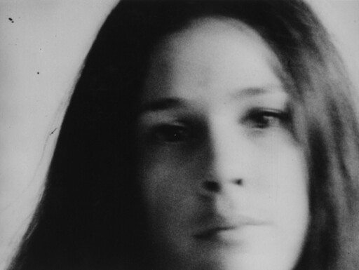 Close-up black-and-white portrait of a young person with long hair and a neutral expression.