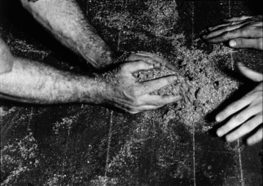 Three hands knead and mix dough on a floured surface, working together to prepare it.