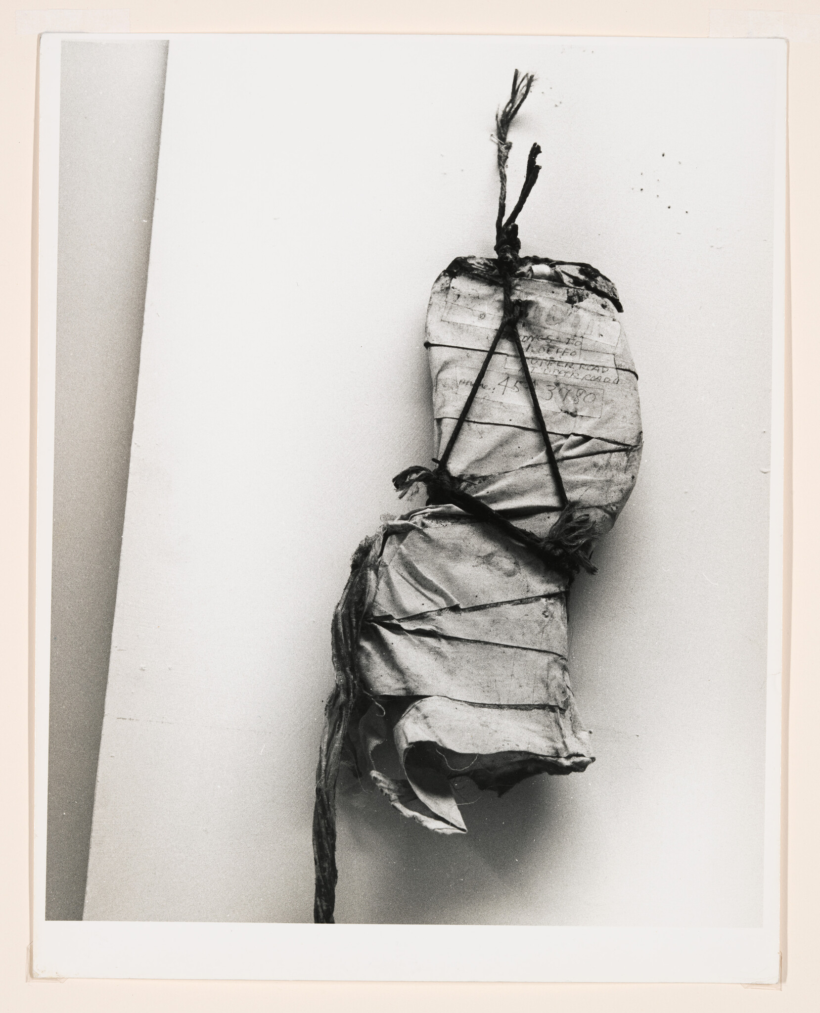 A tattered paper bundle wrapped and tied with string hangs from a nail on a wall.