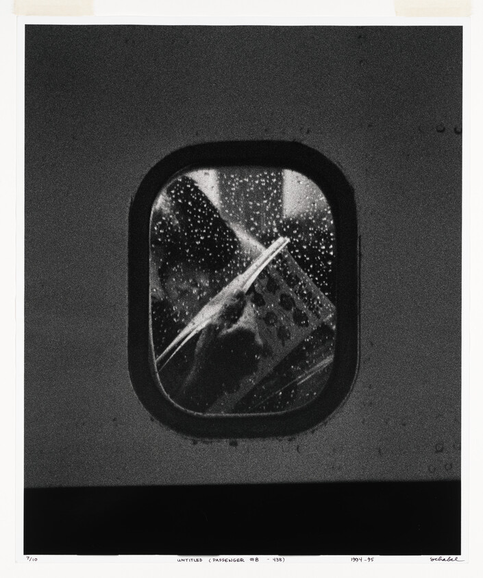 A passenger reads a magazine through a rain-speckled airplane window.