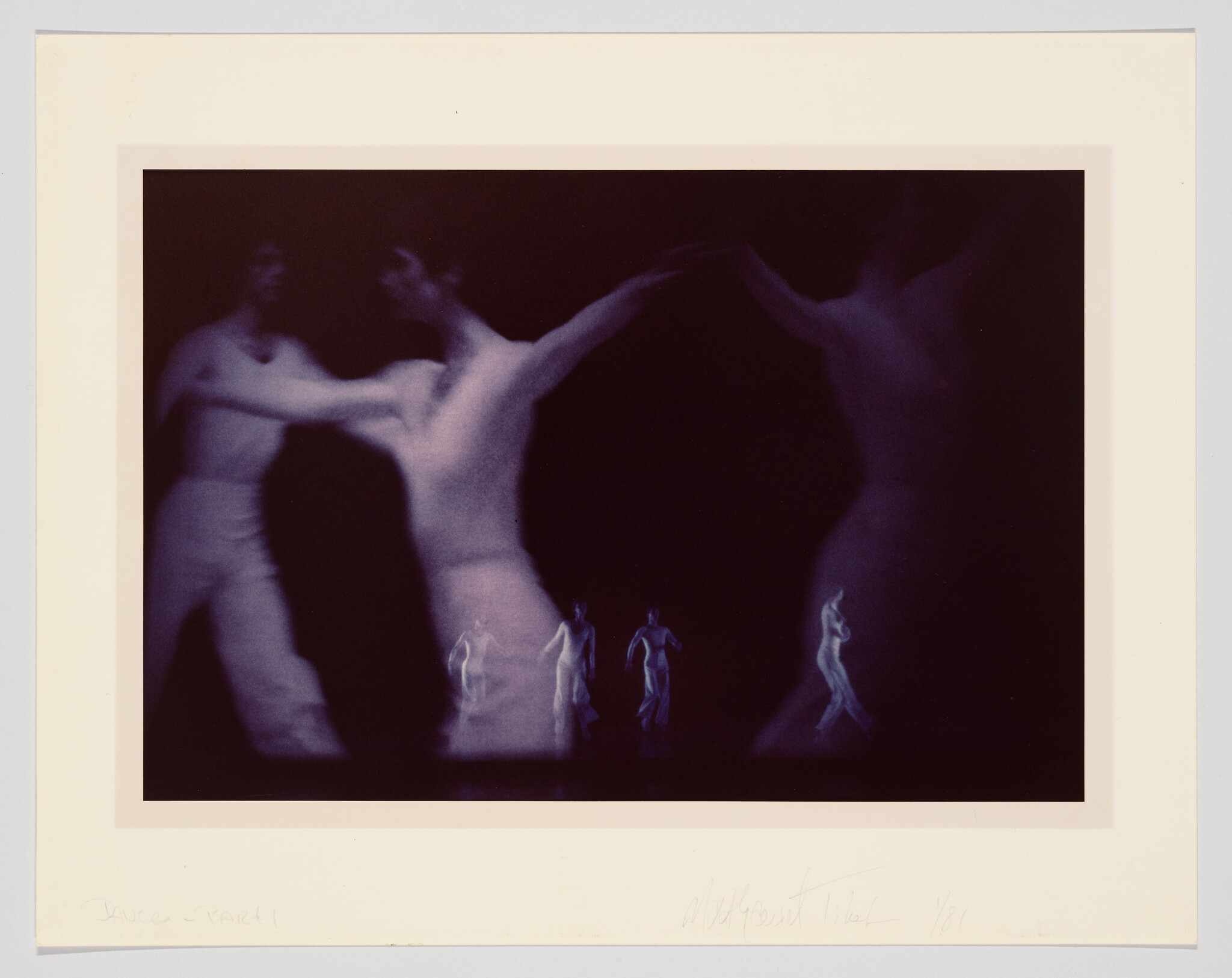 A photograph capturing a blurred motion of dancers in a dark setting, creating a ghostly and ethereal effect. There are multiple figures visible, suggesting movement and dance, with a lighter exposure in the center where two dancers seem to be in contact. The image is bordered by a white frame with handwritten inscriptions at the bottom.