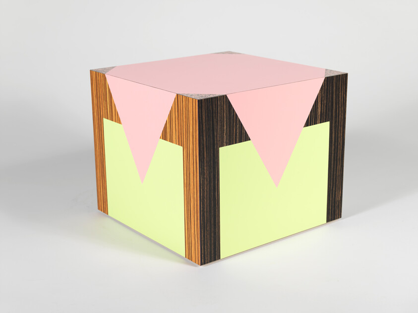 A cube with a wood grain texture on its edges and neon-colored geometric shapes on each visible side, featuring a pink triangle on top and green triangles on the sides, against a white background.