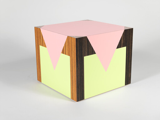 Decorative geometric cube with pink top, yellow side panels, and wood-grain vertical stripes.