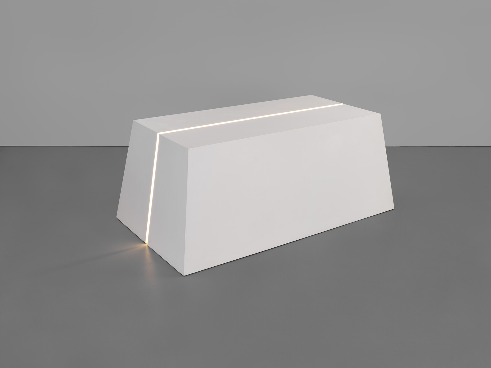A white trapezoid bench with a thin illuminated slit running along its top and front corner.