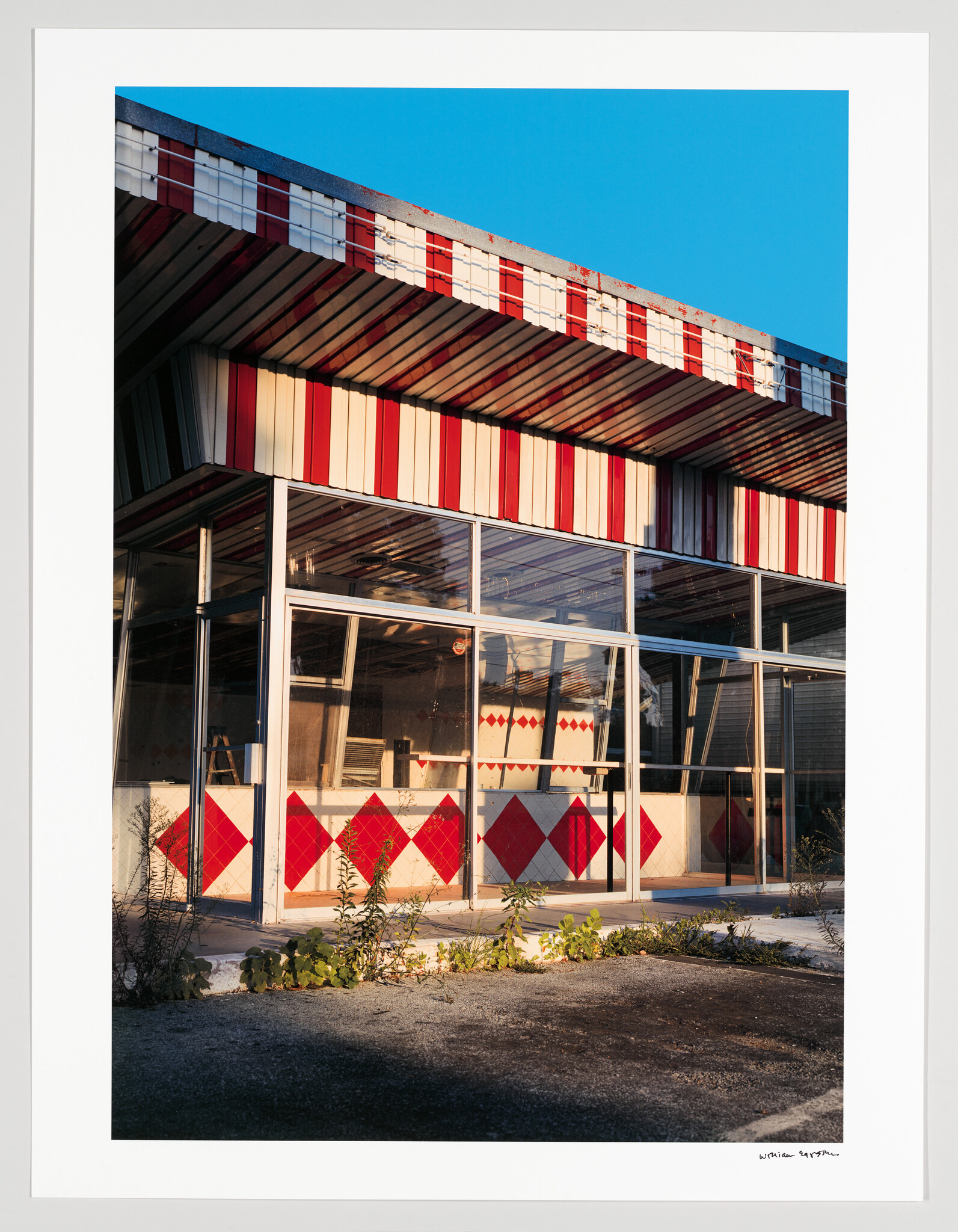 Abandoned red-and-white striped diner with cracked windows and weeds growing in the parking area.