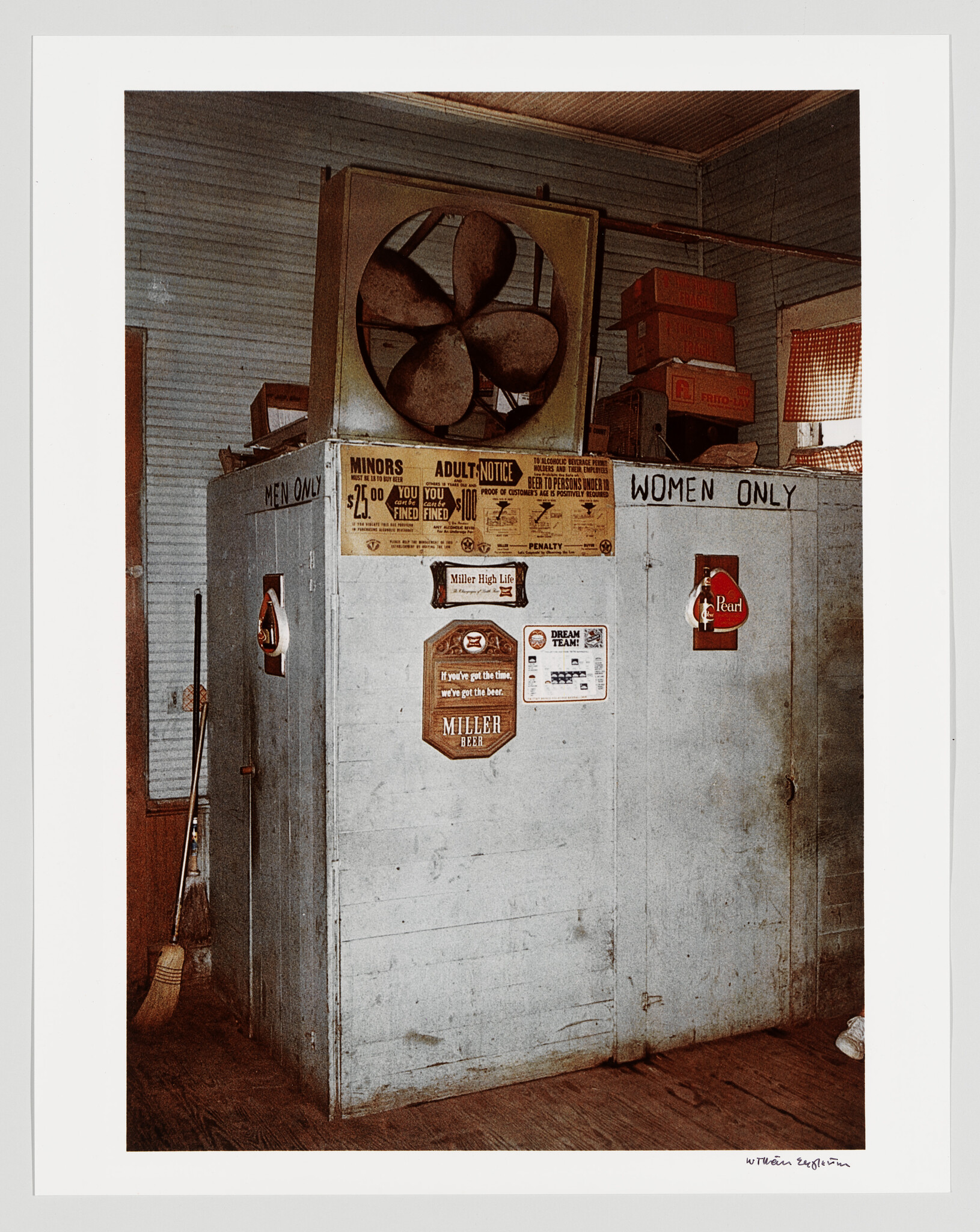 Old wooden restroom booths labeled "Men only" and "Women only" with a large fan and beer signs.