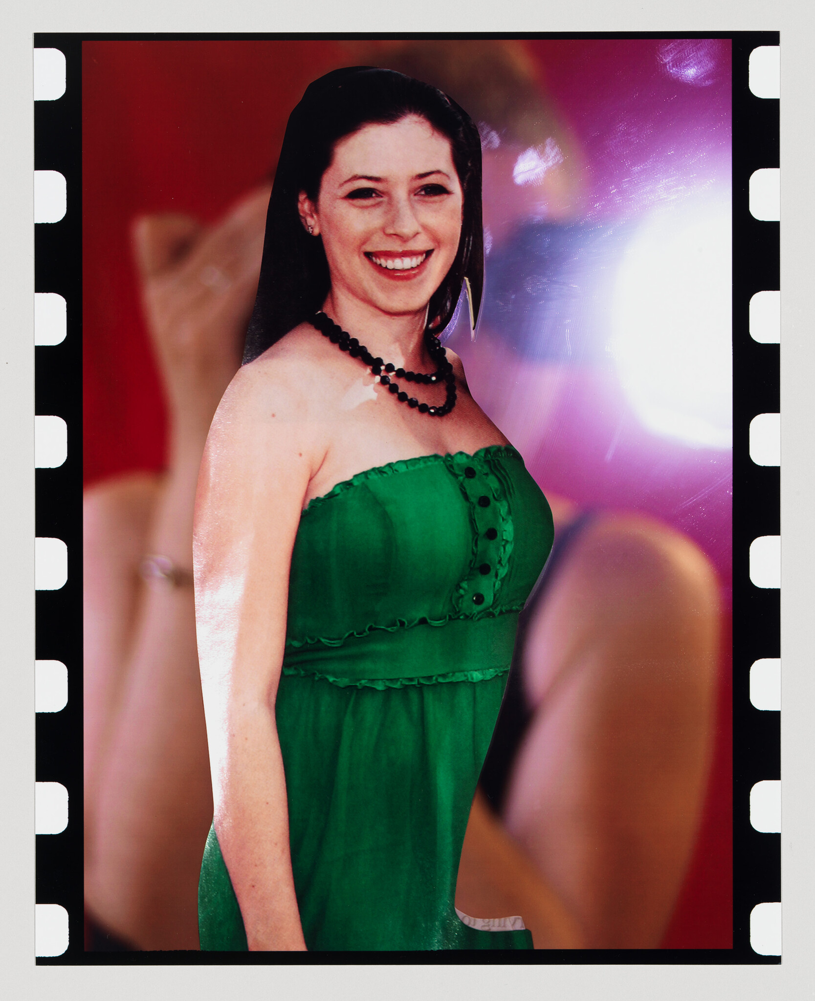 A woman in a green strapless dress smiles at the camera while wearing a black beaded necklace.