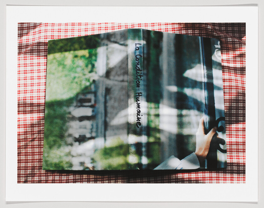 A hardcover book titled "La condition humaine" lies on red checkered fabric with a hand nearby.