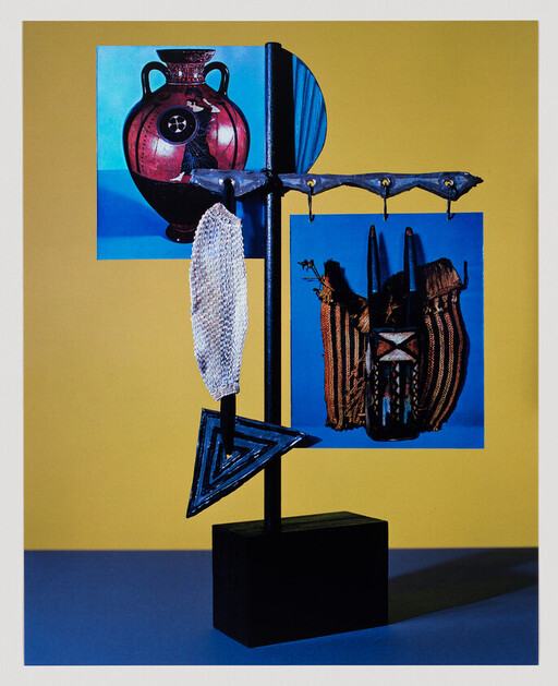 Metal stand displays hanging tribal mask, woven bag, shell and triangular pendant against yellow background.