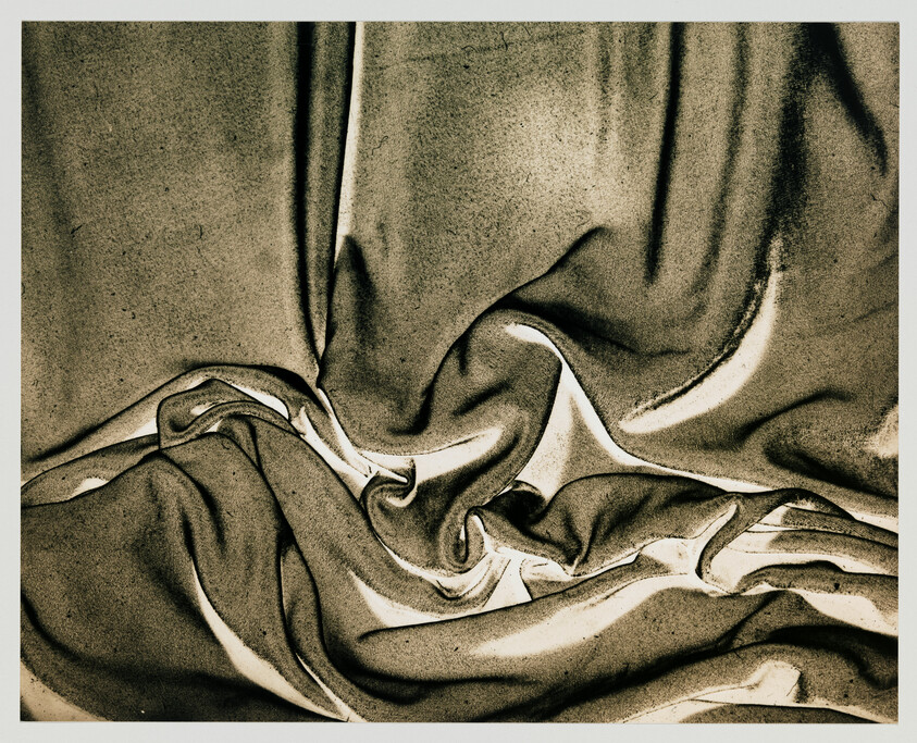 Dark, silky fabric drapes in smooth, flowing folds with highlighted creases and deep shadows.