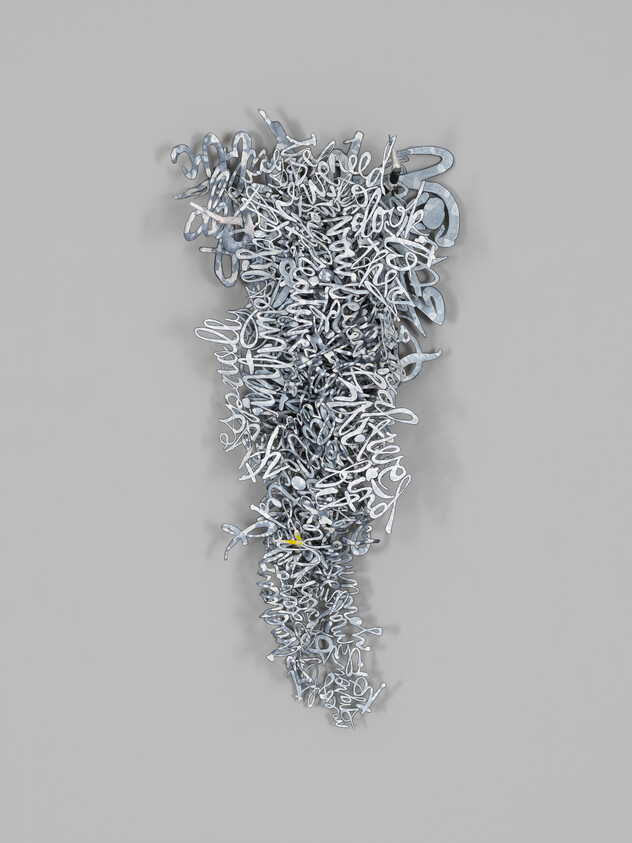 A cascading cluster of silver metallic script letters hangs on a plain gray wall.