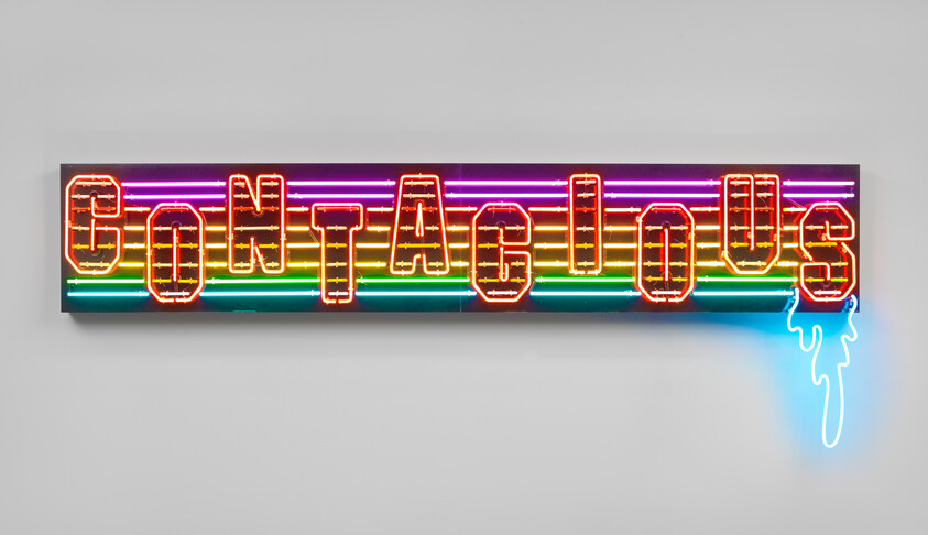 A colorful neon sign mounted on a wall spelling out the word "Contagious" with each letter glowing in a different color. The sign has a melting effect on the last letter with a drip of neon light extending downward.