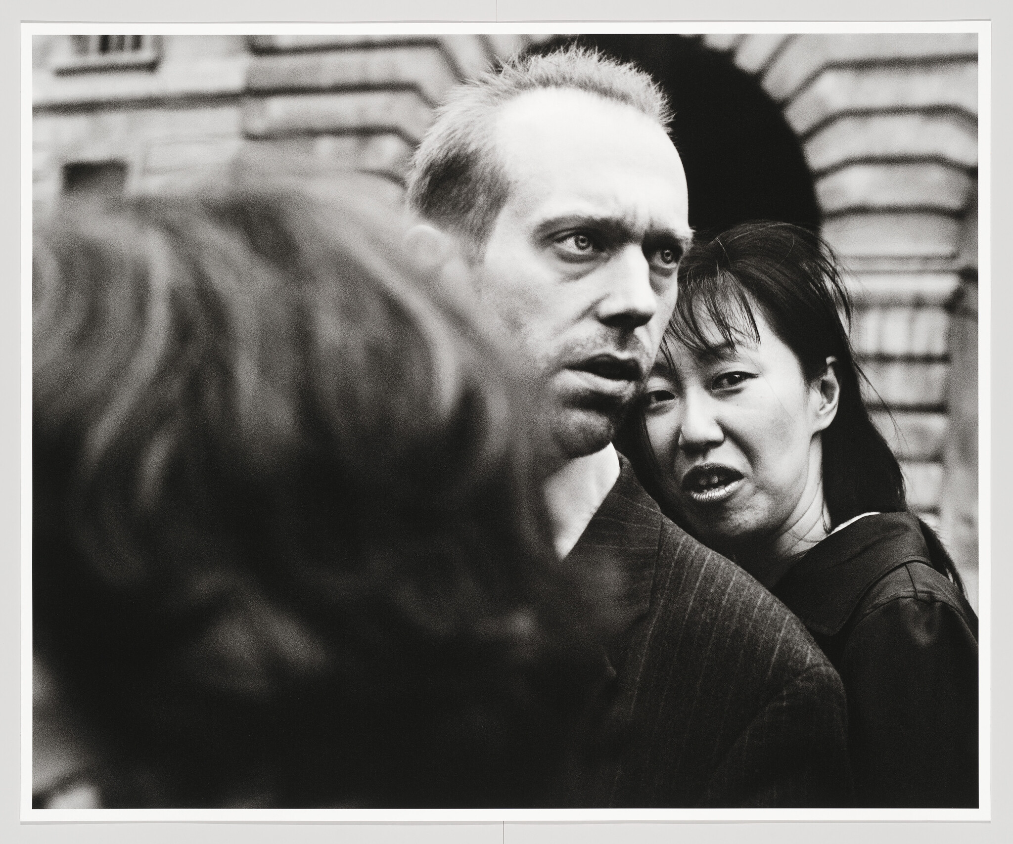 A man looks tense in a crowded street while a woman stands closely behind him.