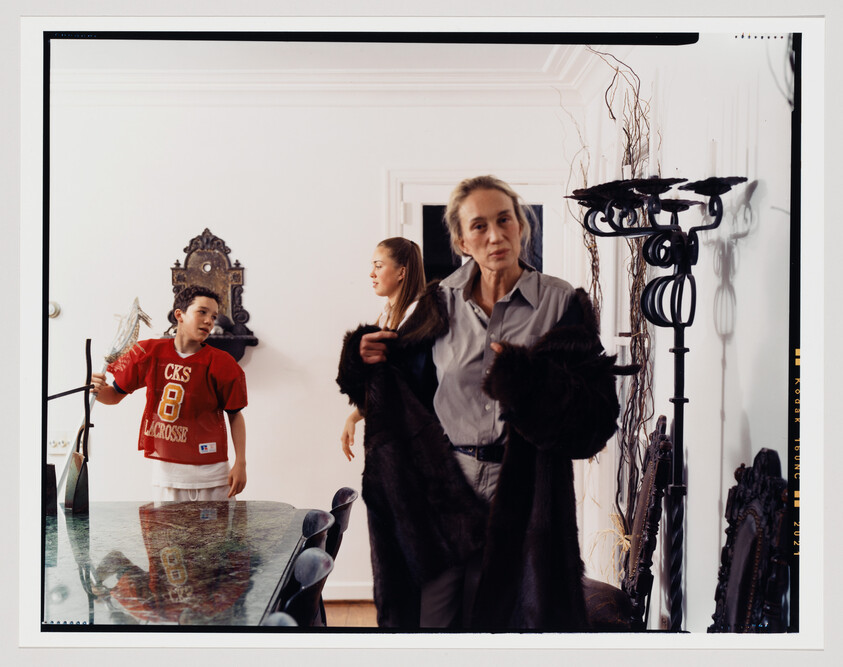 An older woman adjusts a dark fur coat while two younger people stand behind her.