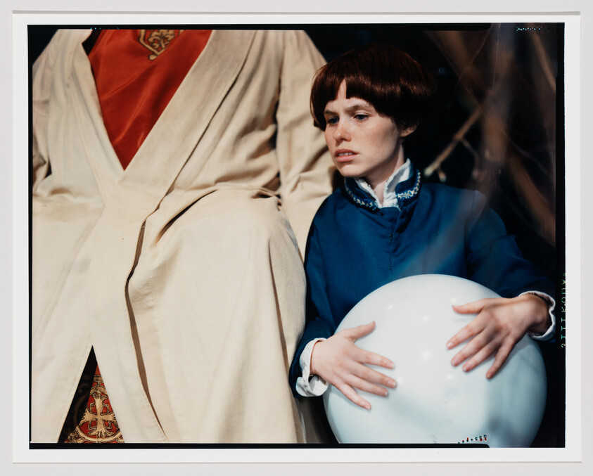 Young person in blue clothing sits beside a robed figure, holding a large white orb.