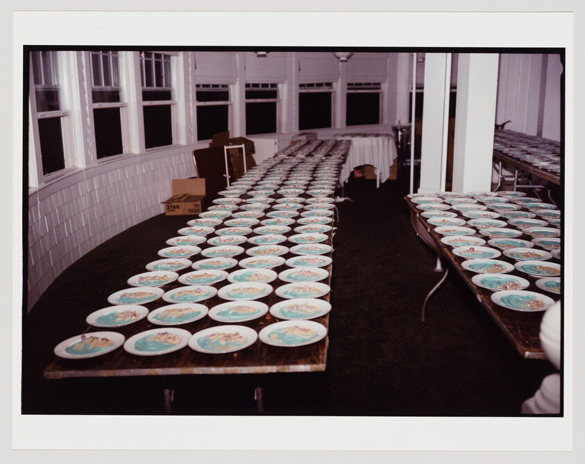 Rows of plates with food arranged on tables in a room with white tiled walls and multiple windows.